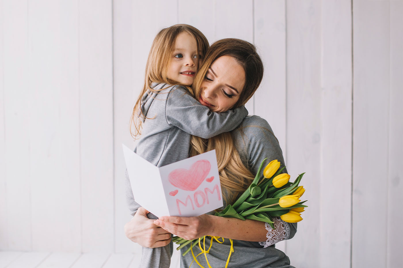 Mamá e hija abrazadas con flores amarillas y una tarjeta