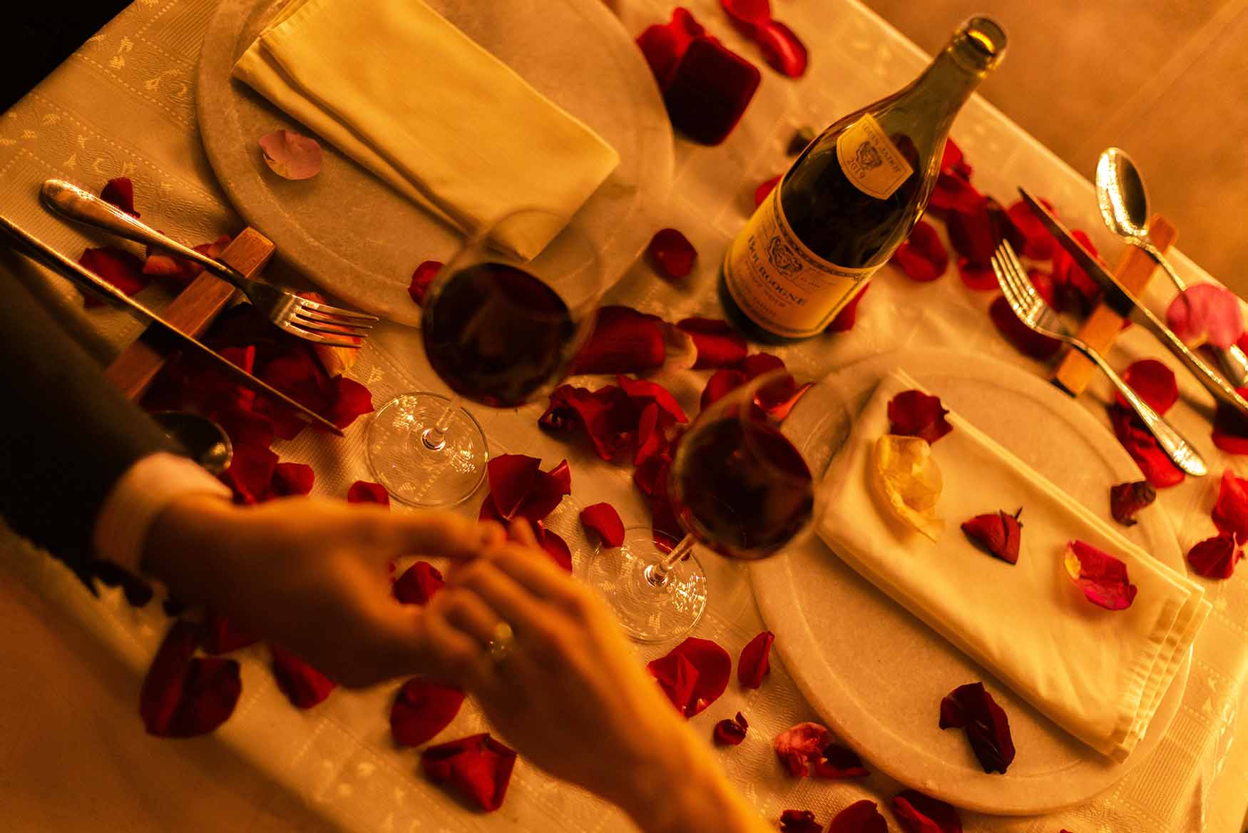 Cena romántica con pétalos de rosa y botella de vino.