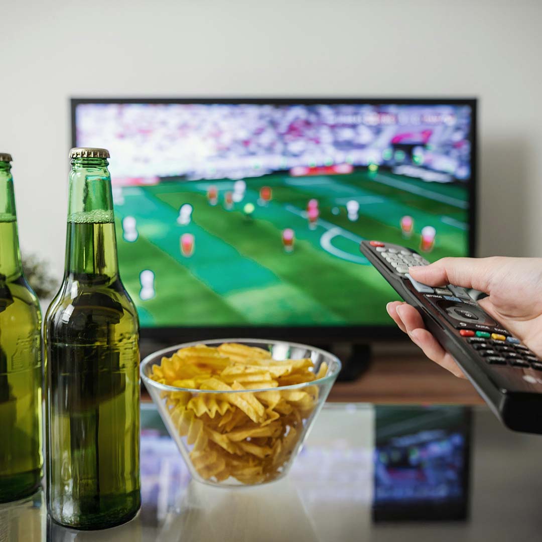 Control de TV, botana, cerveza y TV encendida.