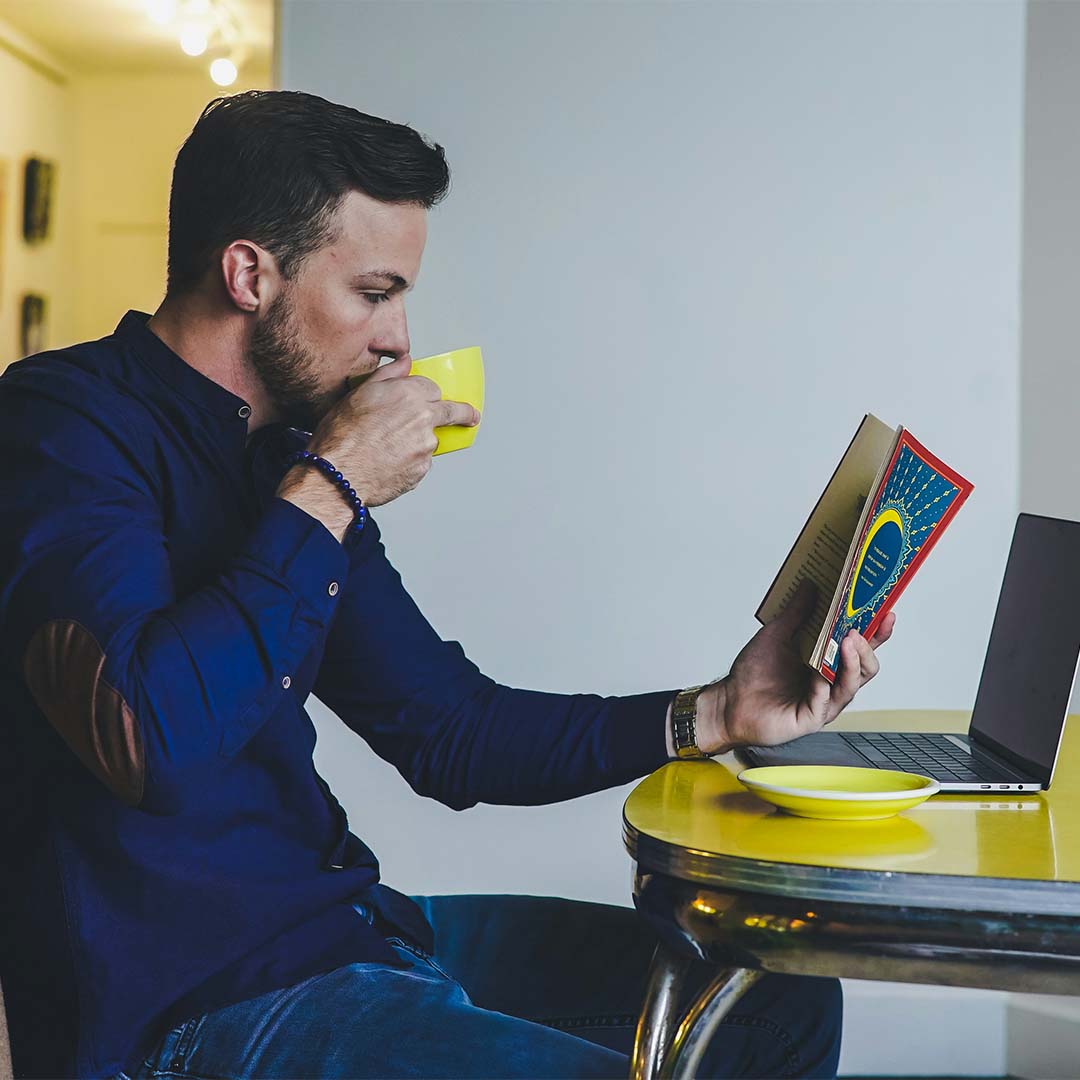 Un hombre lee un libro mientras toma café.