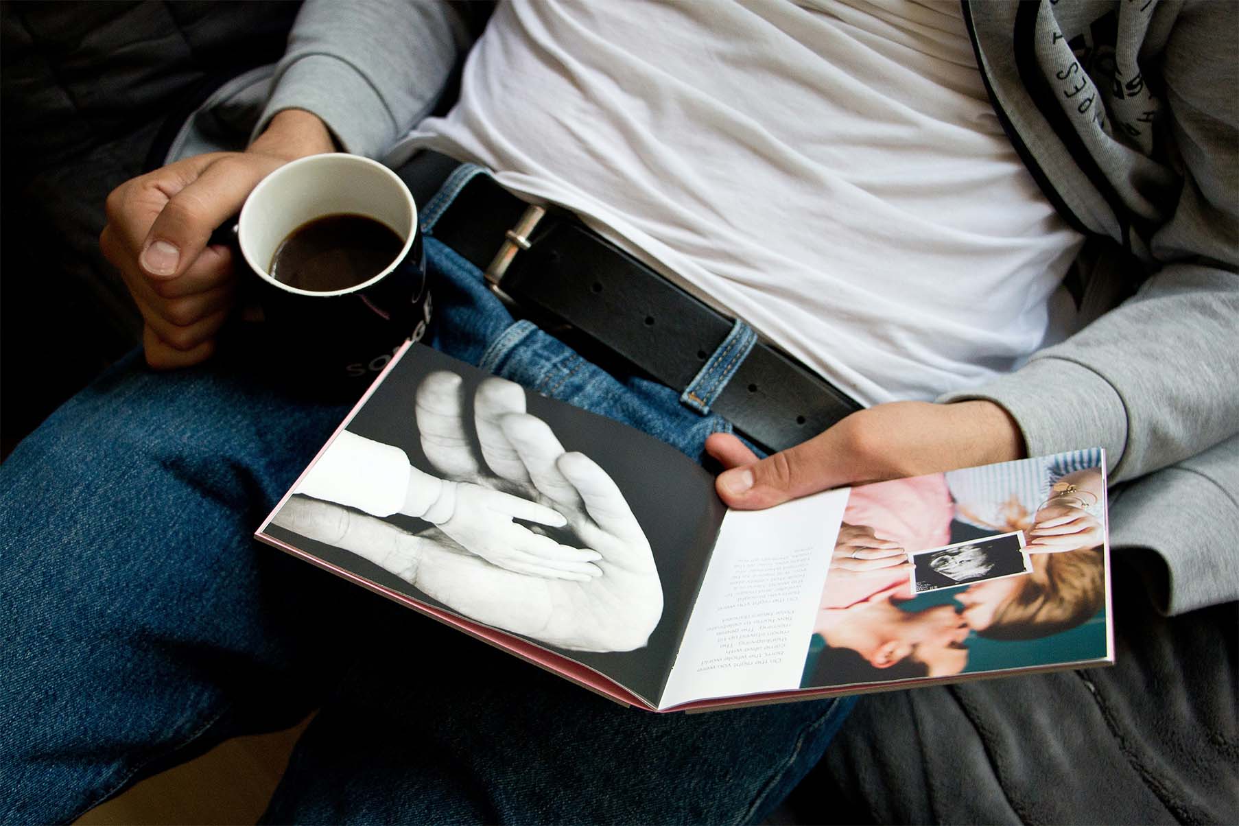 Hombre sostiene un photobook de embarazo y una taza de café.