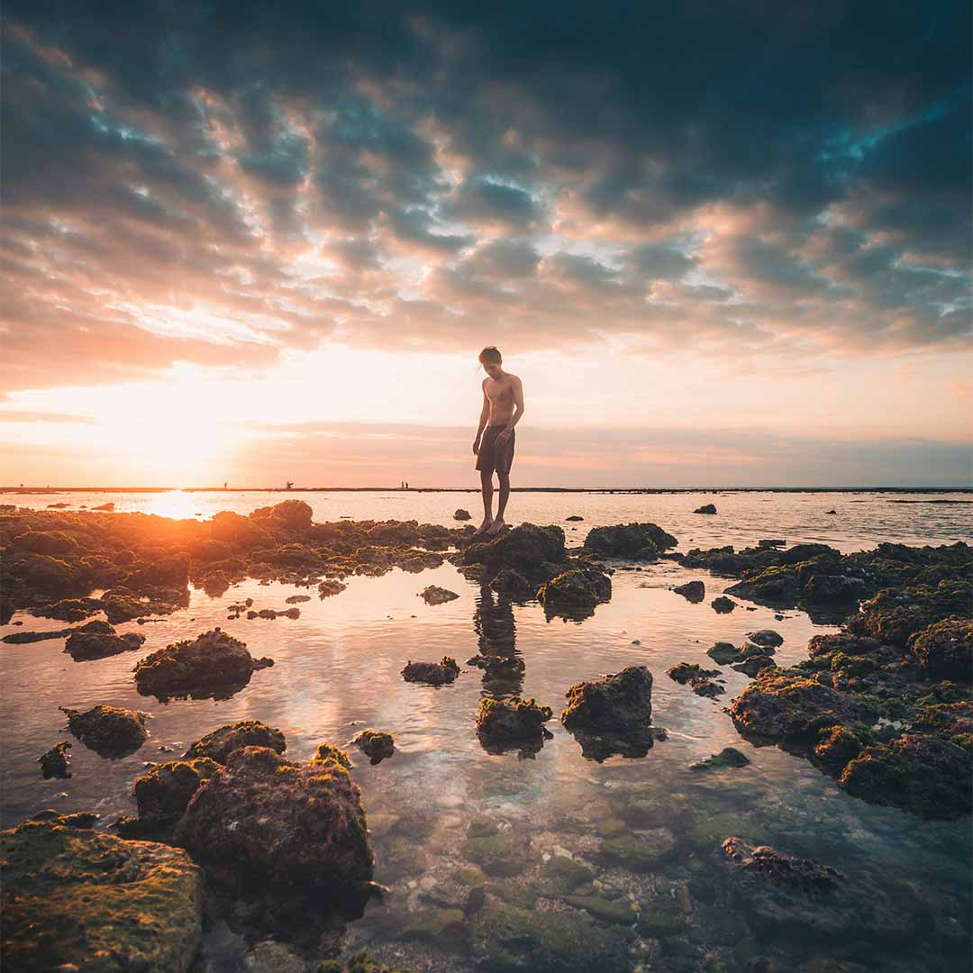 Hombre en la playa con puesta de sol al fondo.