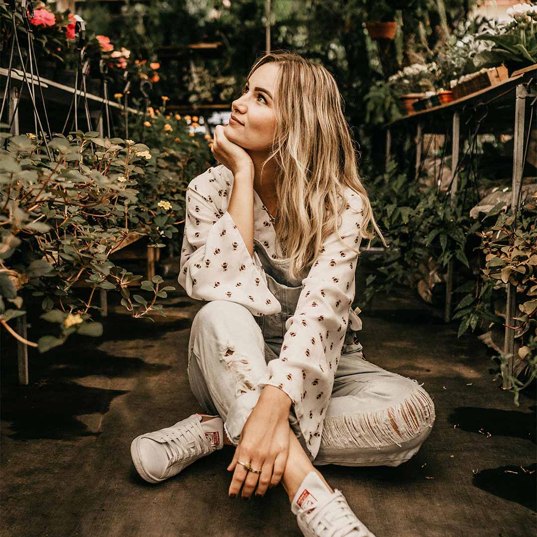 Mujer posando con plantas al fondo.